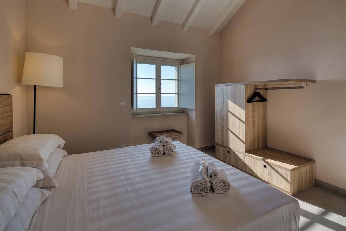 A bedroom with a bed, a bedside table, a lamp, a window, and a wooden wardrobe.