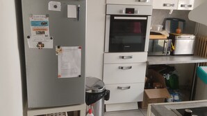 Een compacte keuken met een Bosch oven, een koelkast en een klein aanrecht met diverse spullen.