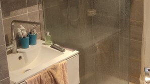 Een badkamer met een douche met glazen wand, een wastafel met toiletartikelen en een handdoek aan de deur.