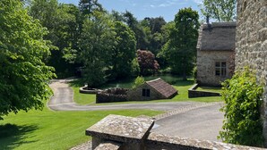 A stone building with a thatched roof, surrounded by lush greenery and a pond.