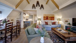 A spacious living area with a high ceiling, wooden beams, a chandelier, and a dining area with wooden chairs and a table.