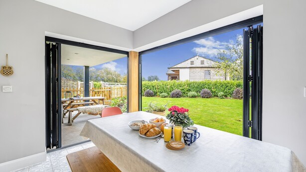 Ontbijttafel met croissants, sinaasappelsap en koffie, voor een grote schuifglazen deur die uitkomt op een tuin.