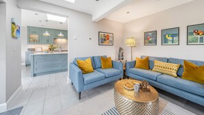 Een moderne woonkamer met een blauwe zithoek, een ronde salontafel en een keuken op de achtergrond.