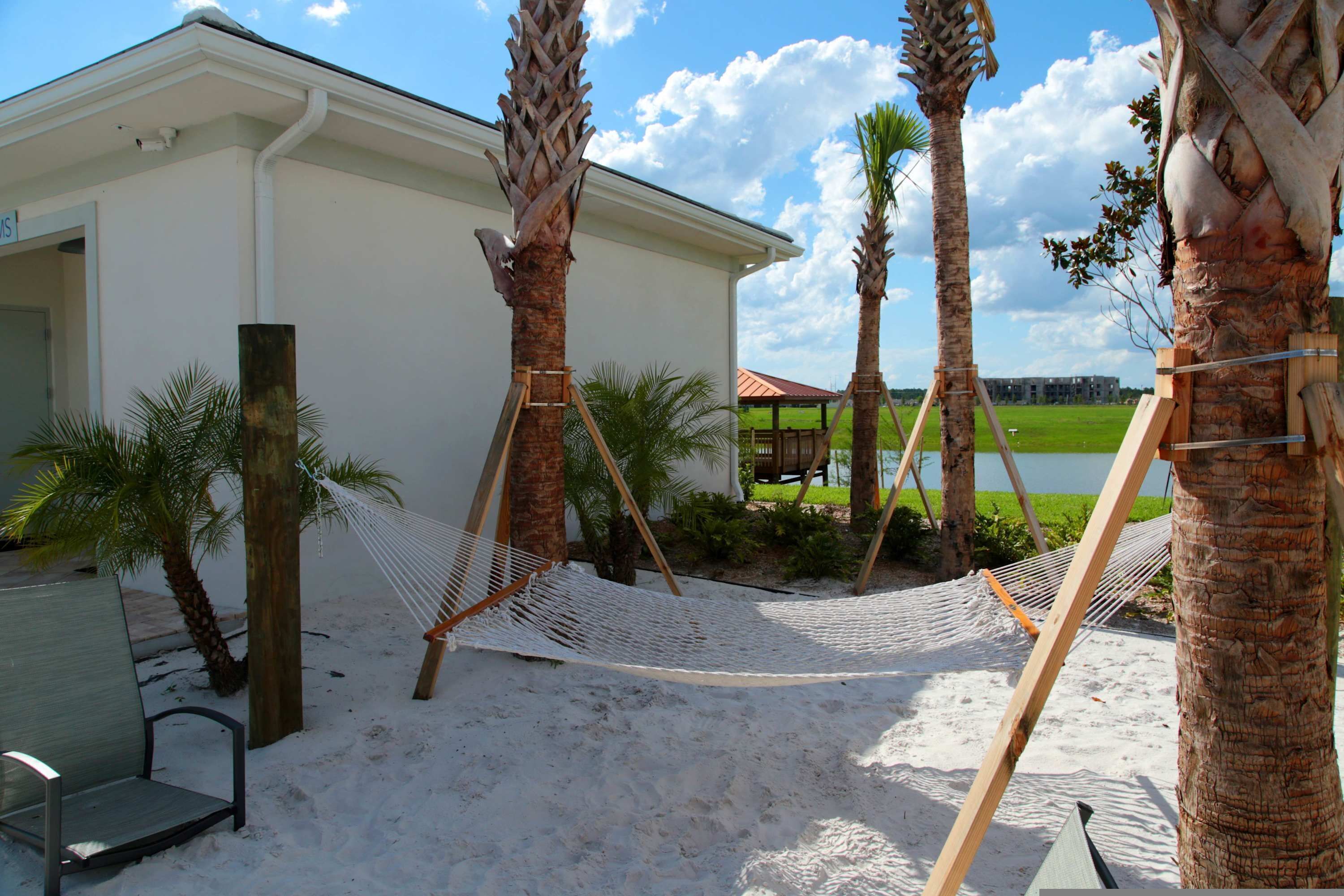 A beach area with a hammock, palm trees, and a building with a sign.