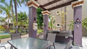 An outdoor patio with a glass table and chairs, a barbecue grill, and a pool in the background. - Coral Luxe Resort - 9 Pools Gym BBQ (Westcourt)