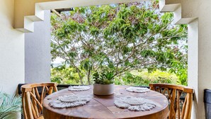 A round wooden table with a potted plant in the center, surrounded by wooden chairs with a view of lush greenery through a window. - Coral Luxe Resort - 9 Pools Gym BBQ (Westcourt)