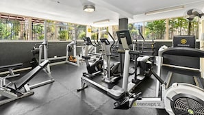 A gym with various exercise equipment, including treadmills and weight machines, and large windows offering views of greenery. - Coral Luxe Resort - 9 Pools Gym BBQ (Westcourt)