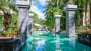 Una piscina con una profundidad de 1,0m, rodeada de palmeras y sillas de descanso.