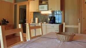 Ett kompakt kök med träskåp, en mikrovågsugn, en kaffebryggare och ett matbord med stolar.