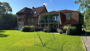 A two-story house with a large front lawn, a balcony, and a satellite dish. - Coastal Comfort With Garden (Fehmarn)