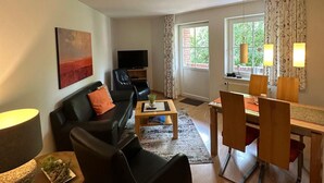 A living room with a black sofa, a coffee table, a TV, and a dining area with chairs and a table. - Coastal Comfort With Garden (Fehmarn)
