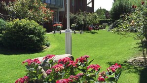 A residential area with a well-maintained lawn, a house with a red brick facade, and a garden with pink flowers. - Coastal Comfort With Garden (Fehmarn)