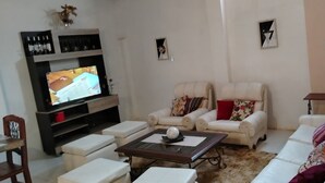 A living room with a sofa, armchairs, a coffee table, a TV, and a bookshelf. - Hostal Deluxe Py offers you comfort, friendliness and (Asunción)