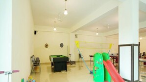 A spacious indoor play area with a pool table, chairs, and a slide. - Pineland Chalets And Resort (Kasauli)