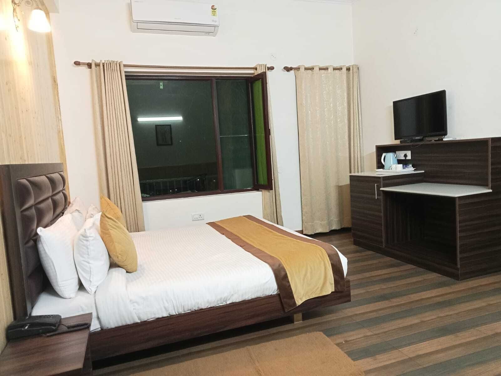 A hotel room with a bed, a desk, a television, and an air conditioning unit.