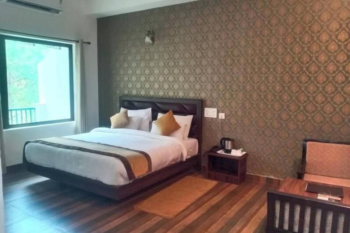 A hotel room with a large bed, a nightstand with a lamp, a window, and a patterned wall.