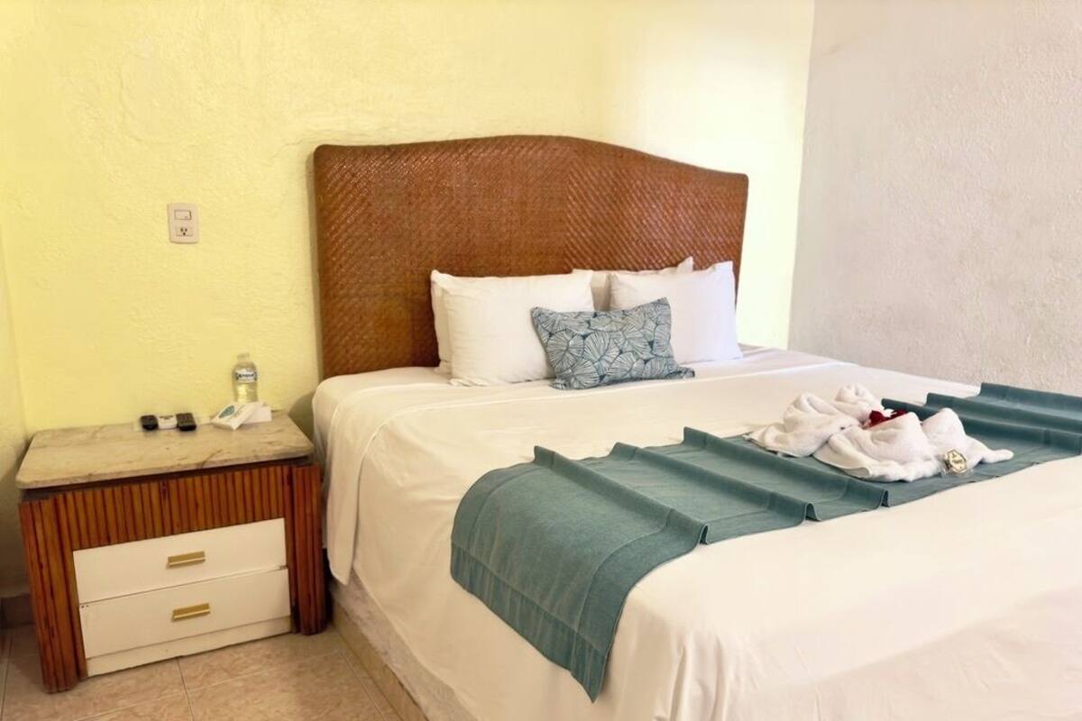 Ein ordentlich bezogenes Bett mit weißen Leinen, einem Holz-Kopfteil und einer blauen Tagesdecke.
