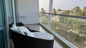 A balcony with a black wicker sofa and white cushions, large windows offering a view of palm trees and buildings. - Modern and Spacious Family Loft with Private Beach / Relax in Cartagena (Cartagena de Indias)