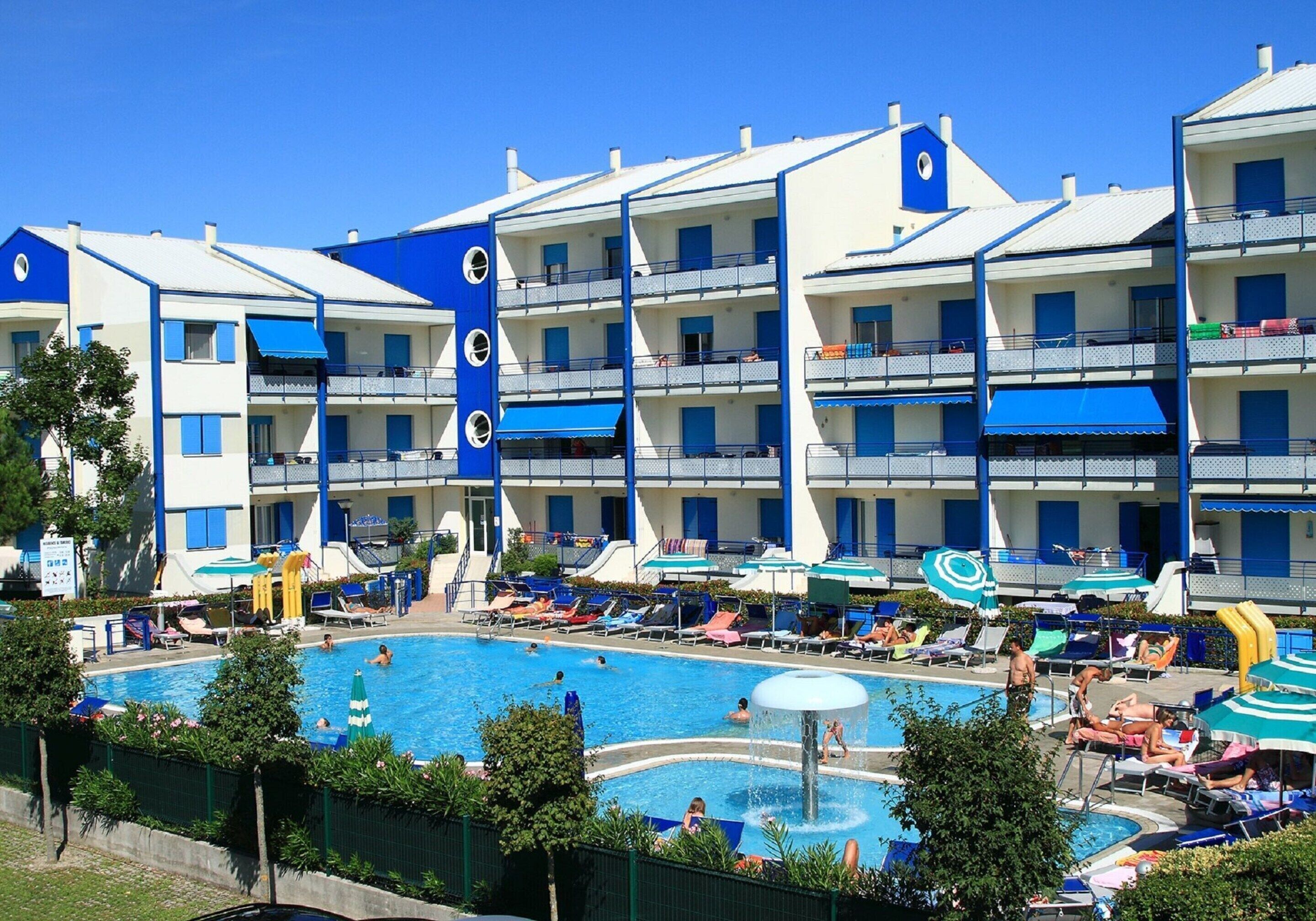 A hotel with multiple balconies, a swimming pool, and sun loungers.