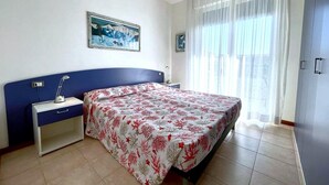 A bedroom with a bed, a nightstand, a desk, a chair, a window with curtains, and a painting on the wall. - Relaxing Coastal Stay in Lido Altanea (Caorle)
