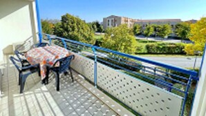A balcony with a table and chairs, a blue railing, and a view of a building and trees. - Relaxing Coastal Stay in Lido Altanea (Caorle)