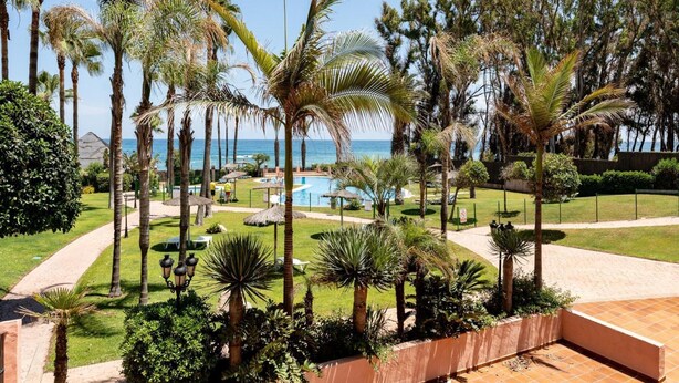 A resort with a pool, palm trees, and a view of the ocean. - Beachfront Apartment -don Juan Manilva (Manilva)