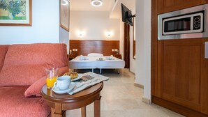 A hotel room with a bed, a TV mounted on the wall, a microwave, a wooden door, and a small table with breakfast items. - Beachfront Apartment -don Juan Manilva (Manilva)