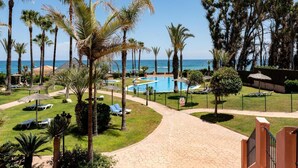 A resort with a swimming pool, palm trees, and a view of the ocean. - Beachfront Apartment -don Juan Manilva (Manilva)