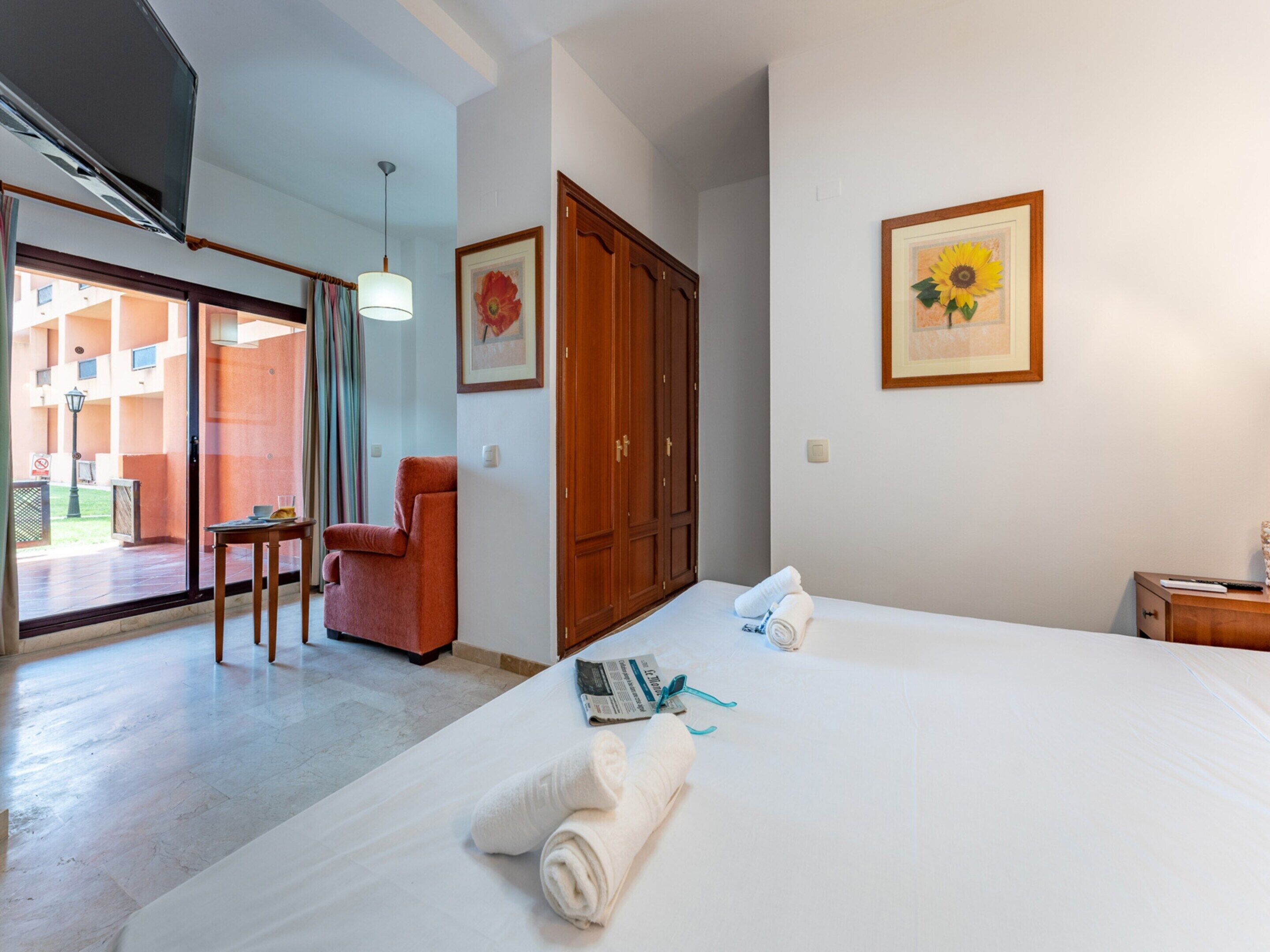 Ein Hotelzimmer mit Bett, Stuhl, Tisch, Schrank und einer Tür zu einem Außenbereich.