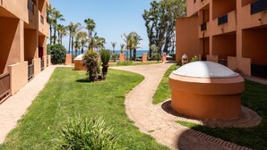 A courtyard with a central circular seating area, surrounded by a pathway, palm trees, and a view of the sea. - Beachfront Apartment -don Juan Manilva (Manilva)