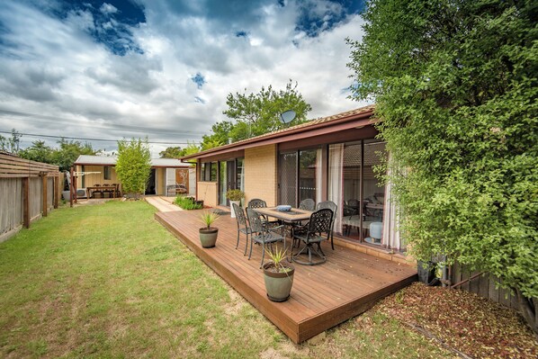 A backyard with a wooden deck, outdoor furniture, and potted plants.
