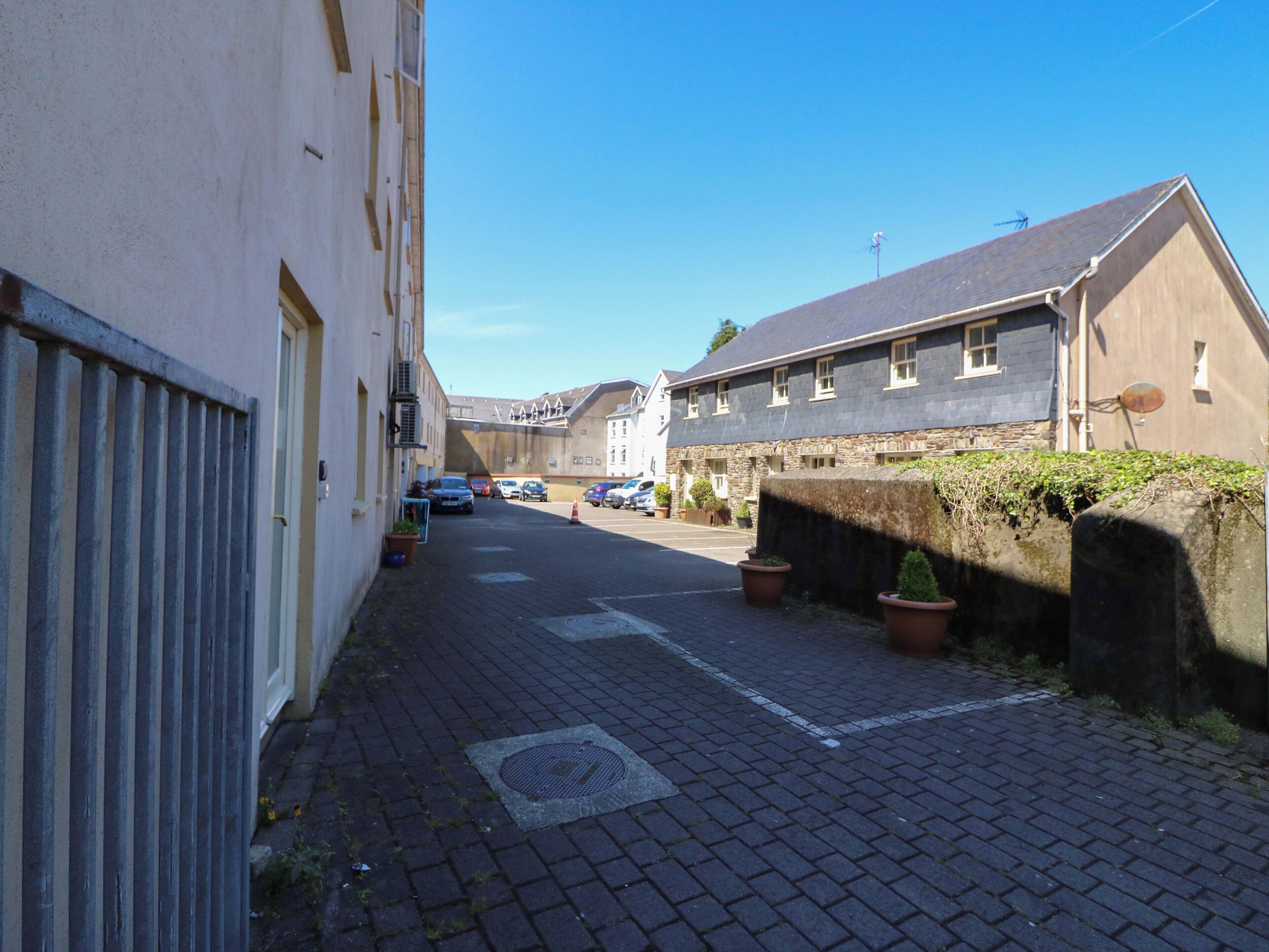 A narrow street with buildings on both sides, a paved road, and parked cars.