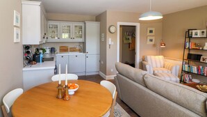A cozy living room with a round wooden table, a beige sofa, and a bookshelf.