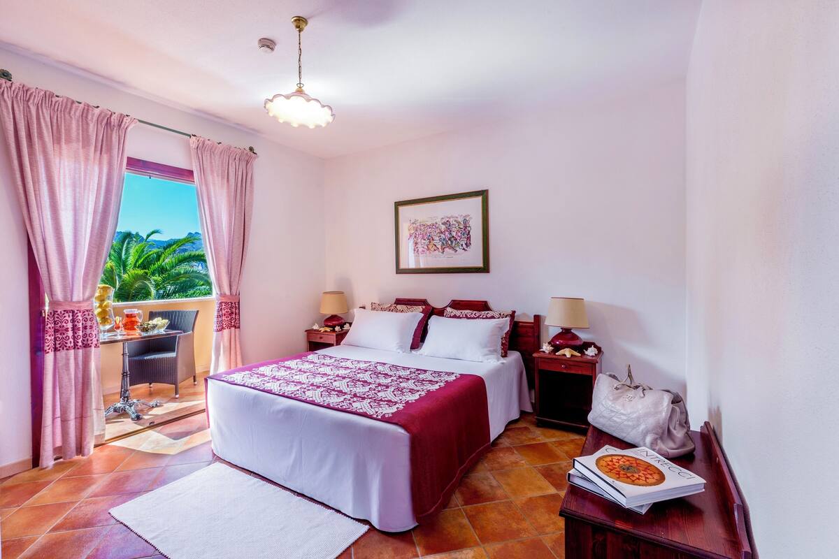 A bedroom with a bed, bedside tables, a lamp, a framed picture, and a view of the outdoors.