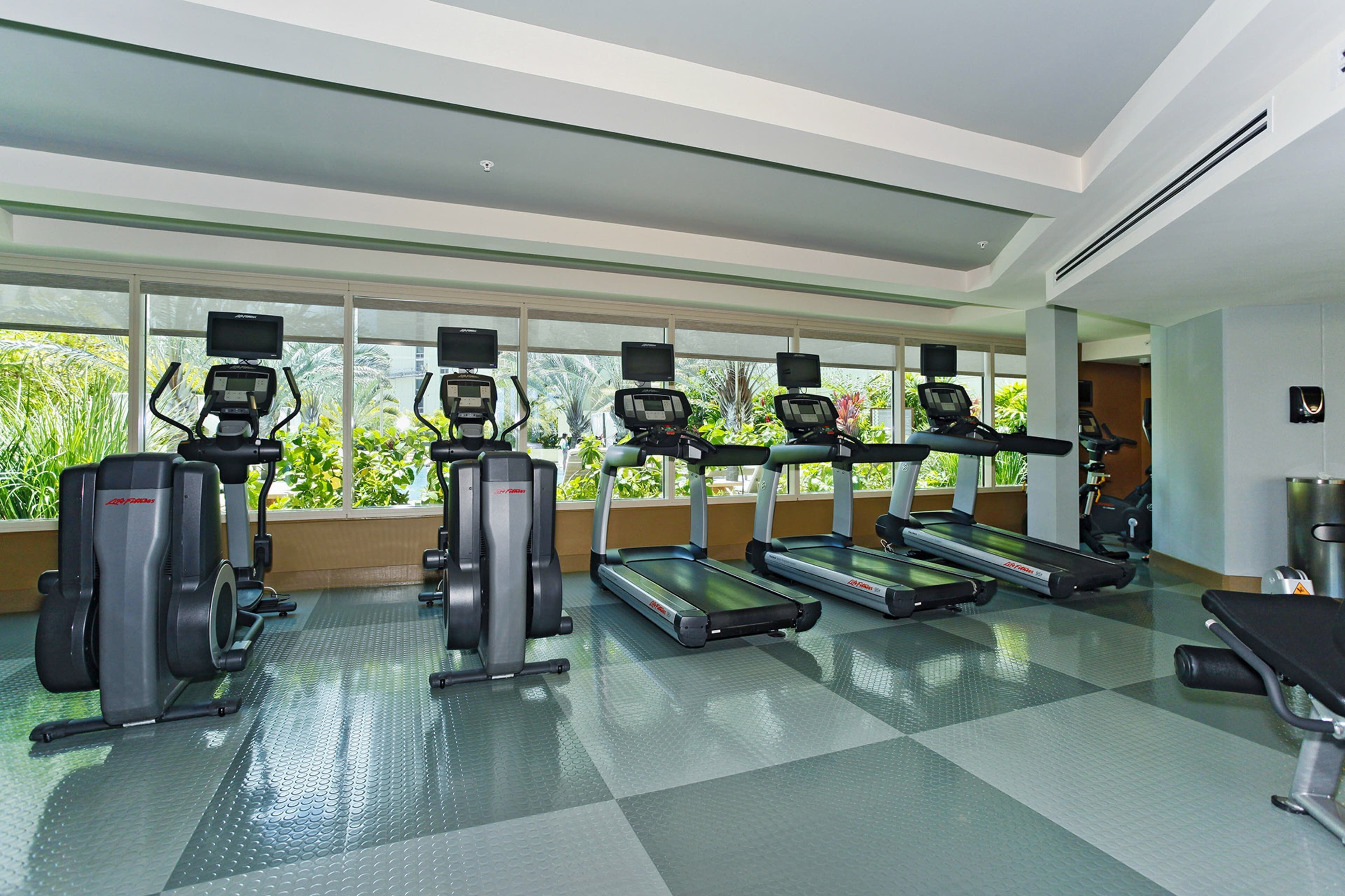 A gym with treadmills, elliptical machines, and a bench.