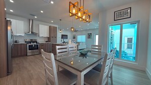 A modern kitchen with stainless steel appliances, a dining area with a glass table, and a view of a balcony.
