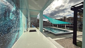 A modern outdoor pool area with a clear view of the pool, a covered seating area, and a view of the surrounding neighborhood.