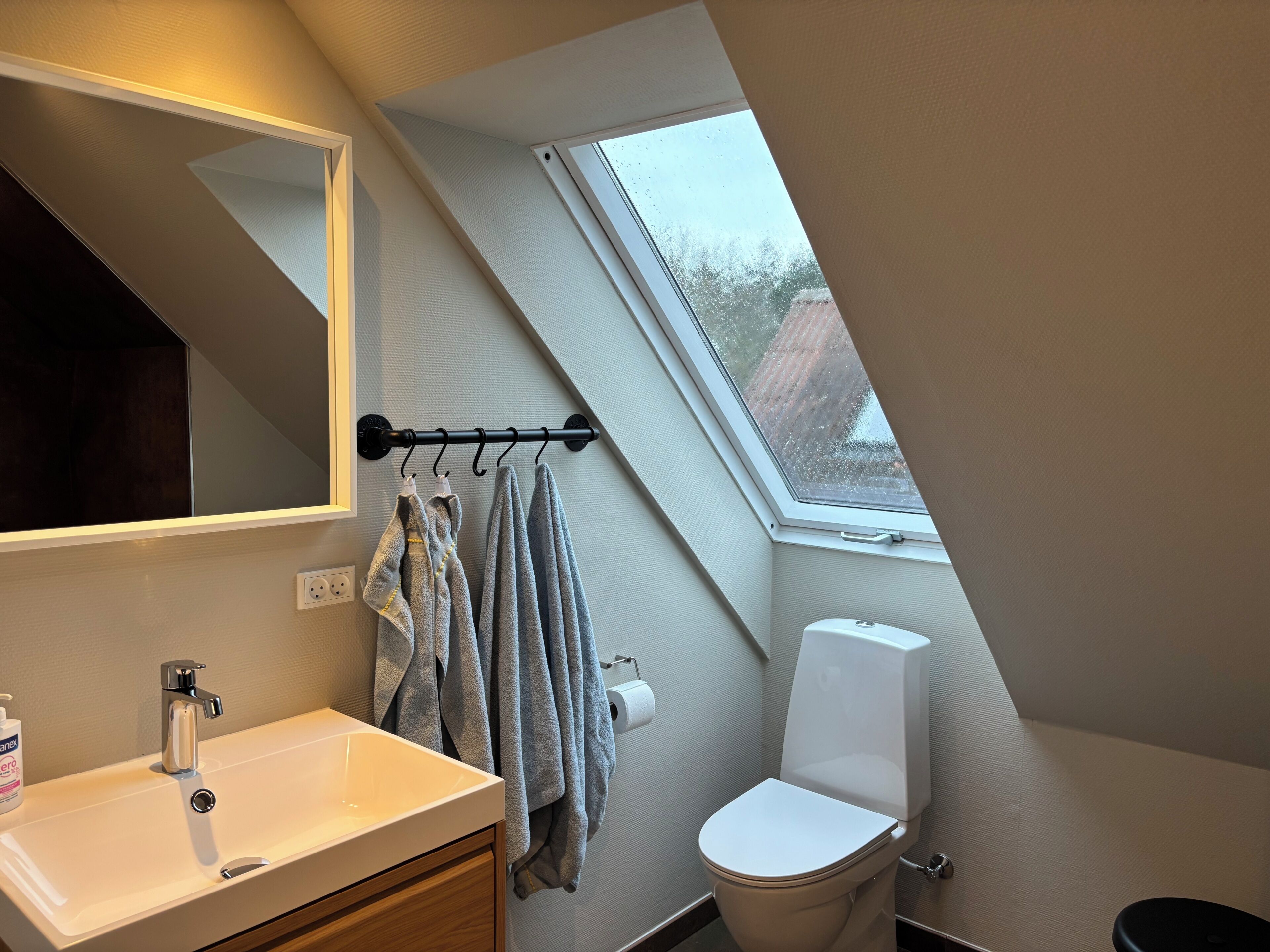 A modern bathroom with a skylight, a white sink, a toilet, and a towel rack.