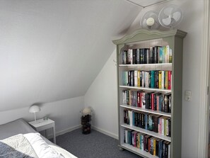Un dormitorio con una estantería, una mesita de noche con lámpara y un pequeño objeto decorativo.