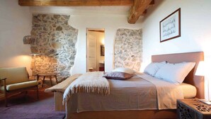 A bedroom with a stone wall, a bed with white linens, a wooden headboard, and a framed picture on the wall. - Casa Leopoldo in Castiglione Chiavarese (Castiglione Chiavarese)