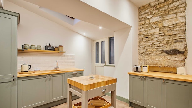 A kitchen with light green cabinets, a wooden countertop, a stone wall, and a window. - Host Stay Temple Terrace (Richmond)