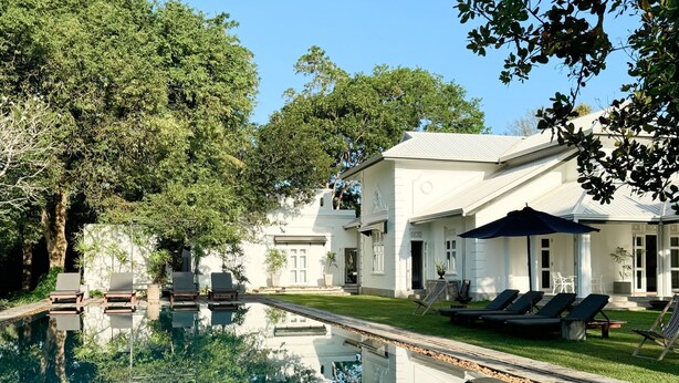 Un grand bâtiment blanc doté d’une piscine, entouré d’arbres et agrémenté d’espaces de détente en plein air.