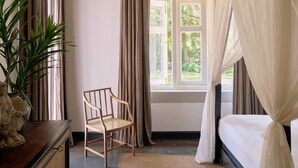 Une chambre à coucher avec un lit, une chaise, une table de chevet, une plante en pot et une fenêtre avec des rideaux.