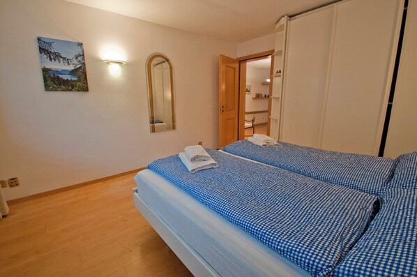 A bedroom with two beds, a wooden floor, a mirror, and a painting on the wall.