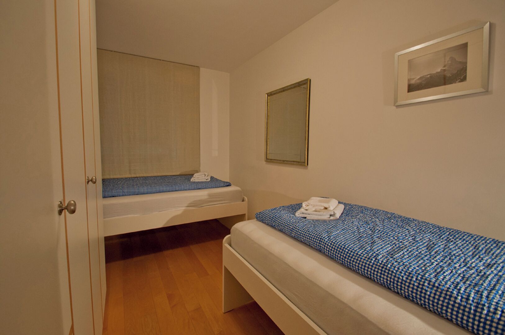 Un petit logement composé d’une seule pièce, comprenant un lit, une table de chevet, un miroir et un tableau encadré accroché au mur.