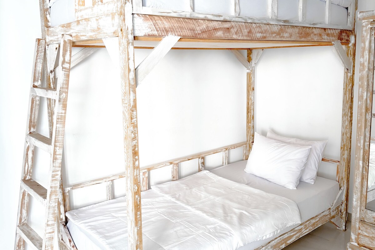 A bunk bed with a ladder, white bedding, and a white wall.