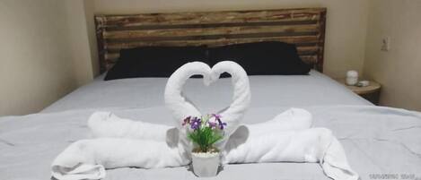 A bed with white linens and a heart-shaped towel arrangement.