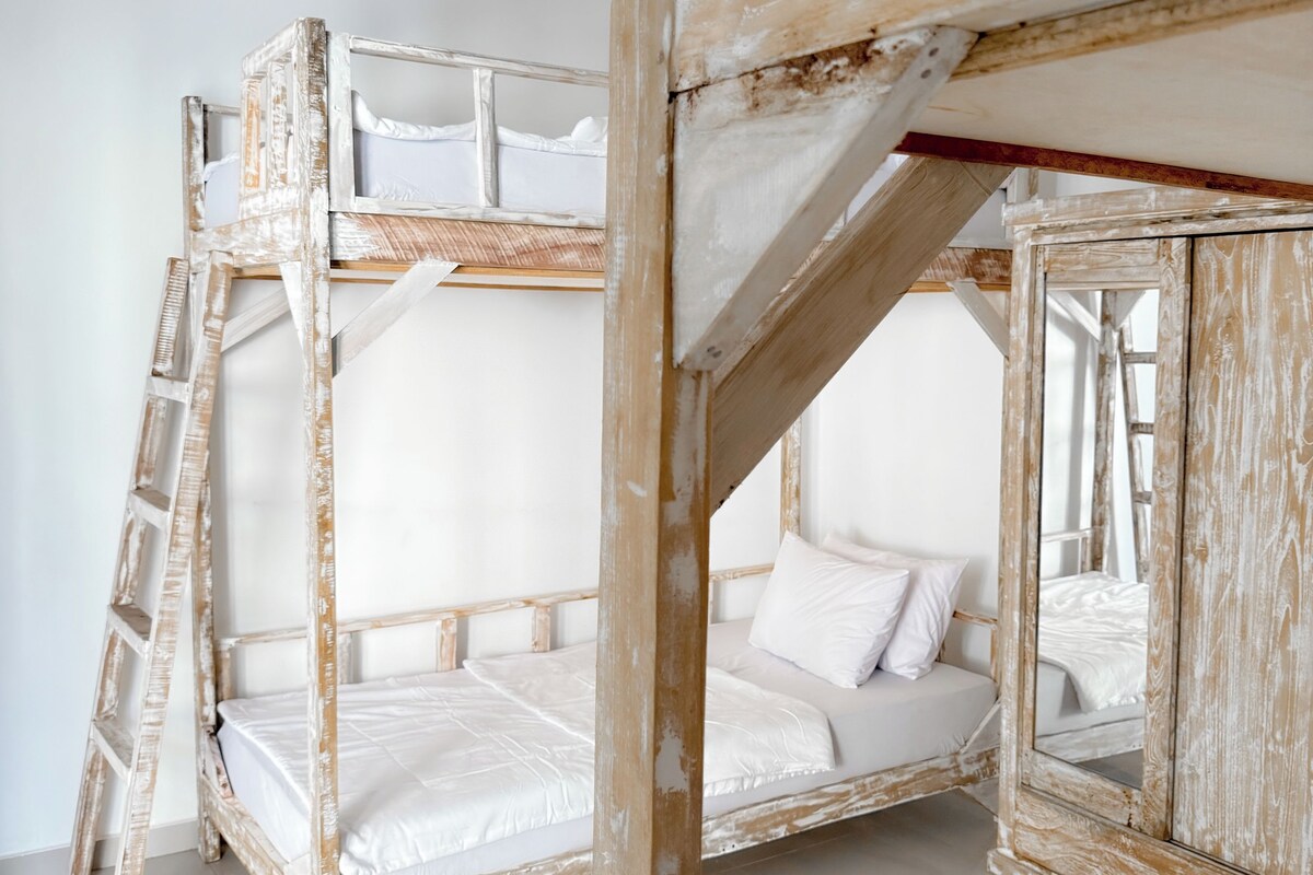 A bunk bed room with a ladder, white bedding, and a mirror reflecting the bed.