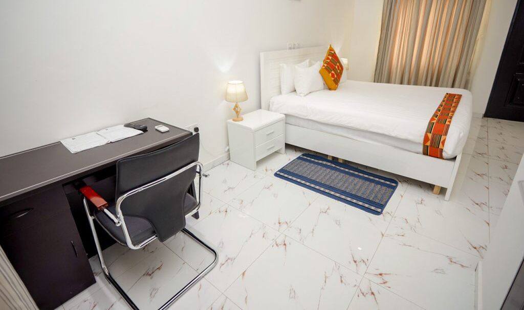 Una habitación de hotel con cama, escritorio, silla, mesita de noche y lámpara.