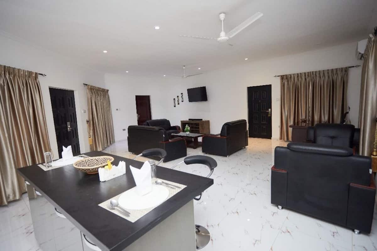 A modern hotel room with a dining area, a sofa set, a TV, and a ceiling fan.